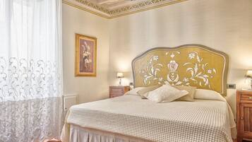 Una camera da letto con un letto grande, una testiera con motivo floreale, due comodini con lampade e una finestra con tende leggere.