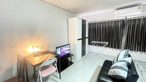 A compact living space with a dining table, a TV, a sofa, and a window with curtains. - Impact Muangthong Condo C3 by Miles (Pak Kret)