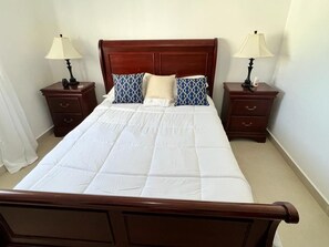 Een keurig opgemaakt bed met een houten hoofdbord, twee nachtkastjes met lampen, en een witte dekbedovertrek.