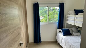 A bedroom with a bunk bed, a window with curtains, and a view of greenery outside. - Las Terrenas Gorgeous Penthouse (Las Terrenas)