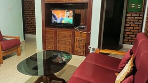 A living room with two red sofas, a glass coffee table, and a television on a wooden cabinet. - Charming 2-Bed House in Kigali (Kigali)