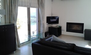 Una sala de estar moderna con un sofá de cuero, un televisor de pantalla plana, una chimenea y un ventanal de vidrio que da a un balcón.
