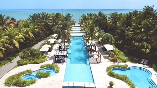 Un complexe hôtelier doté d’une piscine centrale, d’espaces de détente et de palmiers.