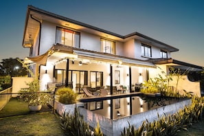 Une maison moderne à deux étages dotée d’un patio couvert, d’un espace salon extérieur et d’une piscine.