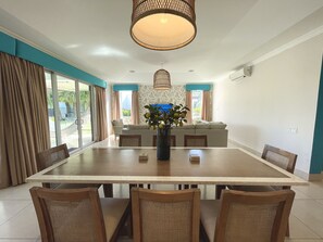 Un coin repas avec une grande table, des chaises, un vase rempli de fleurs et un canapé en arrière-plan.