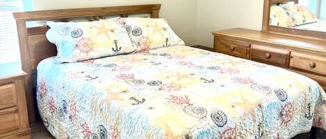 A bedroom with a bed, wooden nightstands, a dresser, a ceiling fan, and a wall-mounted mirror.