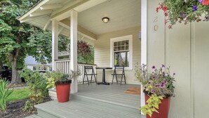 A porch with a wooden railing, a table, and chairs. There are potted plants on either side of the steps. - Third & Lake - Downtown Sandpoint (Sandpoint)