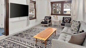 A living room with a flat-screen TV, a wooden coffee table, a grey sofa, and two armchairs with patterned cushions. - Third & Lake - Downtown Sandpoint (Sandpoint)