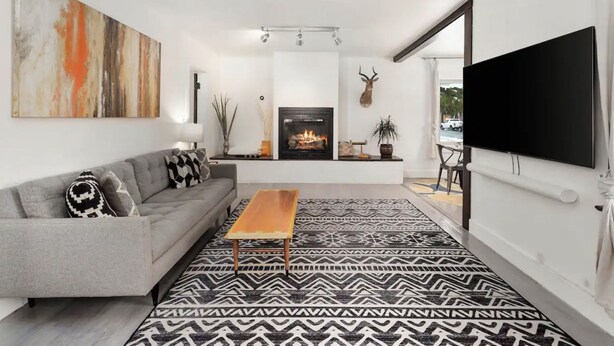 A modern living room with a grey sofa, a wooden coffee table, a patterned rug, a fireplace, and a mounted television. - Third & Lake - Downtown Sandpoint (Sandpoint)