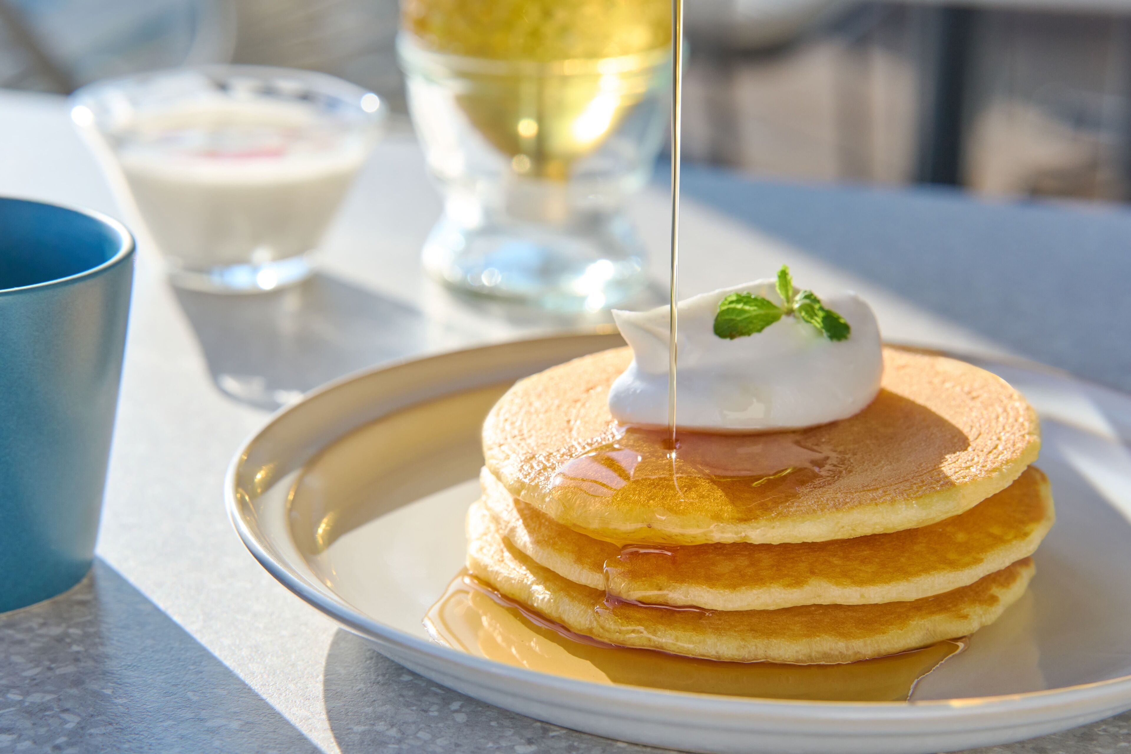 A stack of pancakes with syrup and a dollop of cream on a plate.