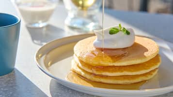 A stack of pancakes with syrup and a dollop of cream on a plate.