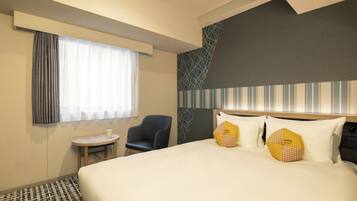 A hotel room with a large bed, a small round table, a chair, and a window with curtains.