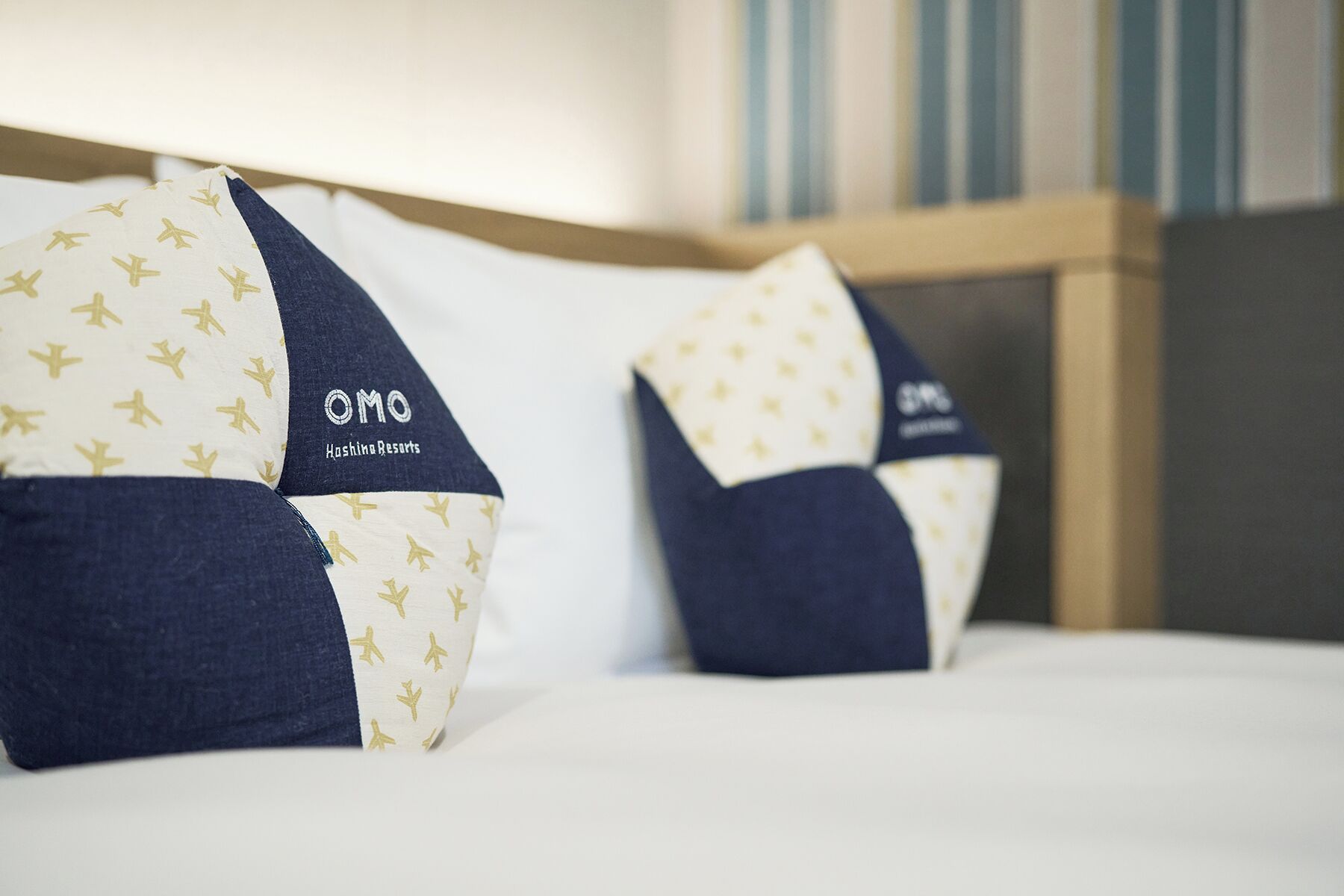Two pillows with a pattern of airplane silhouettes and the text "OMO Hashina Resorts" on a bed.