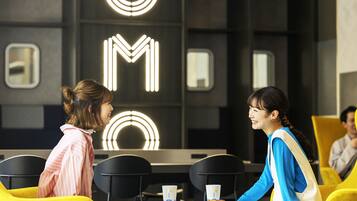 Two people seated at a table with a neon sign in the background.