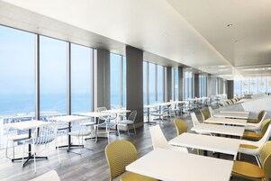 A modern dining area with large windows, white tables, and yellow chairs.