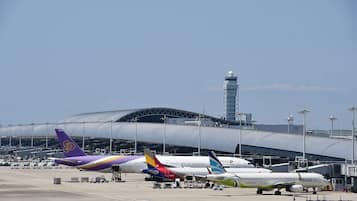 An airport with multiple airplanes parked, a large terminal building, and a control tower in the background.
