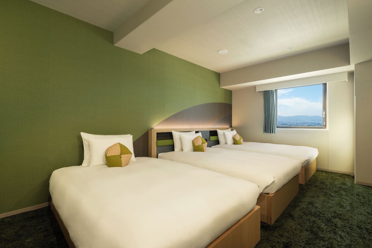 Ein Hotelzimmer mit zwei Betten, einem großen Fenster und Blick auf die Stadt.