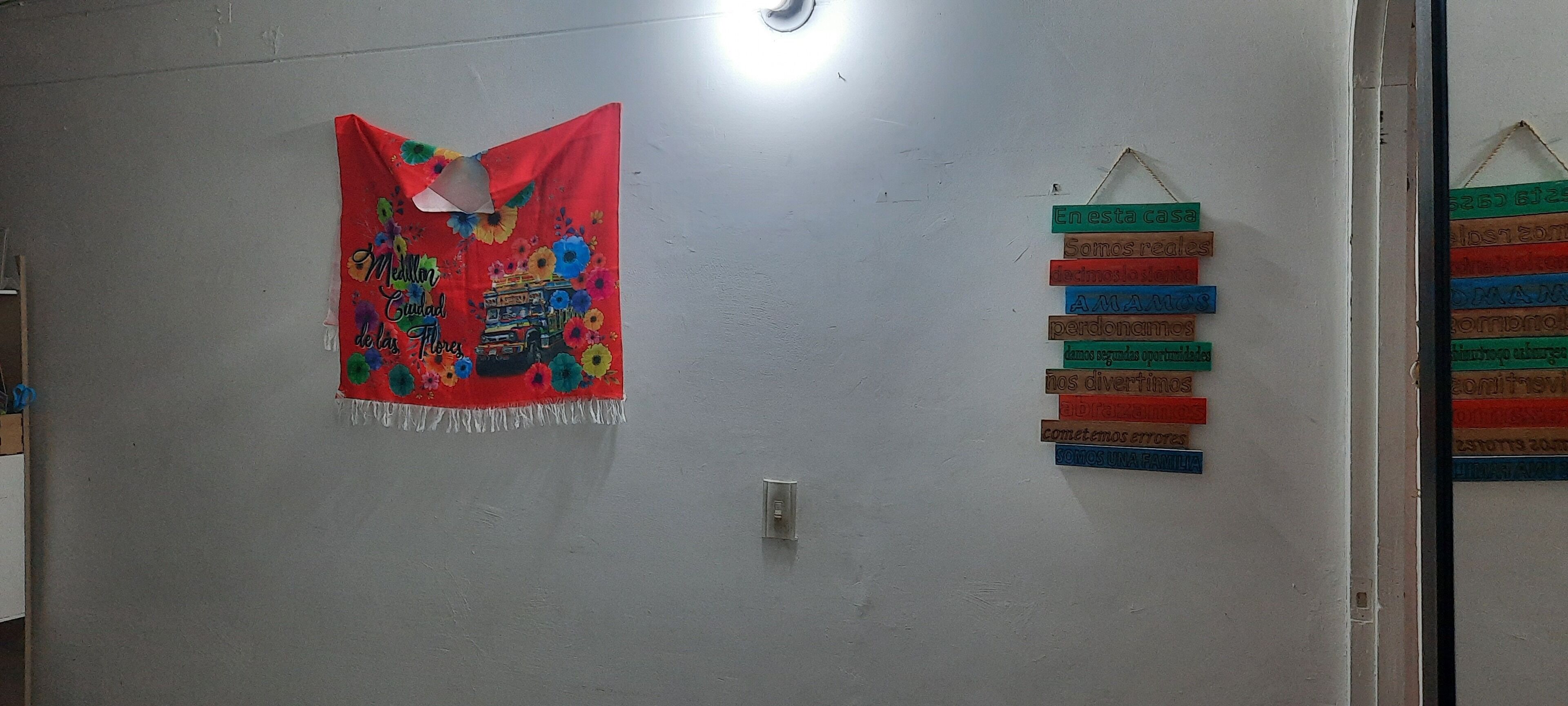 Una habitación con un adorno rojo colgado en la pared, un aparato de iluminación y un letrero en la pared con varios colores.