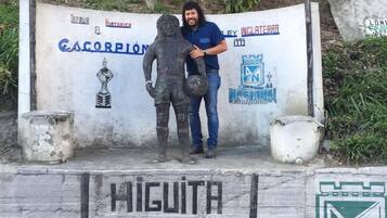 Un hombre está de pie junto a una estatua sobre un pedestal con un cartel que muestra el año 1989 y el nombre "HIGUITA".