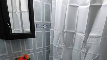 Un baño con inodoro azul, cortina de ducha blanca y un espejo sobre el lavabo.