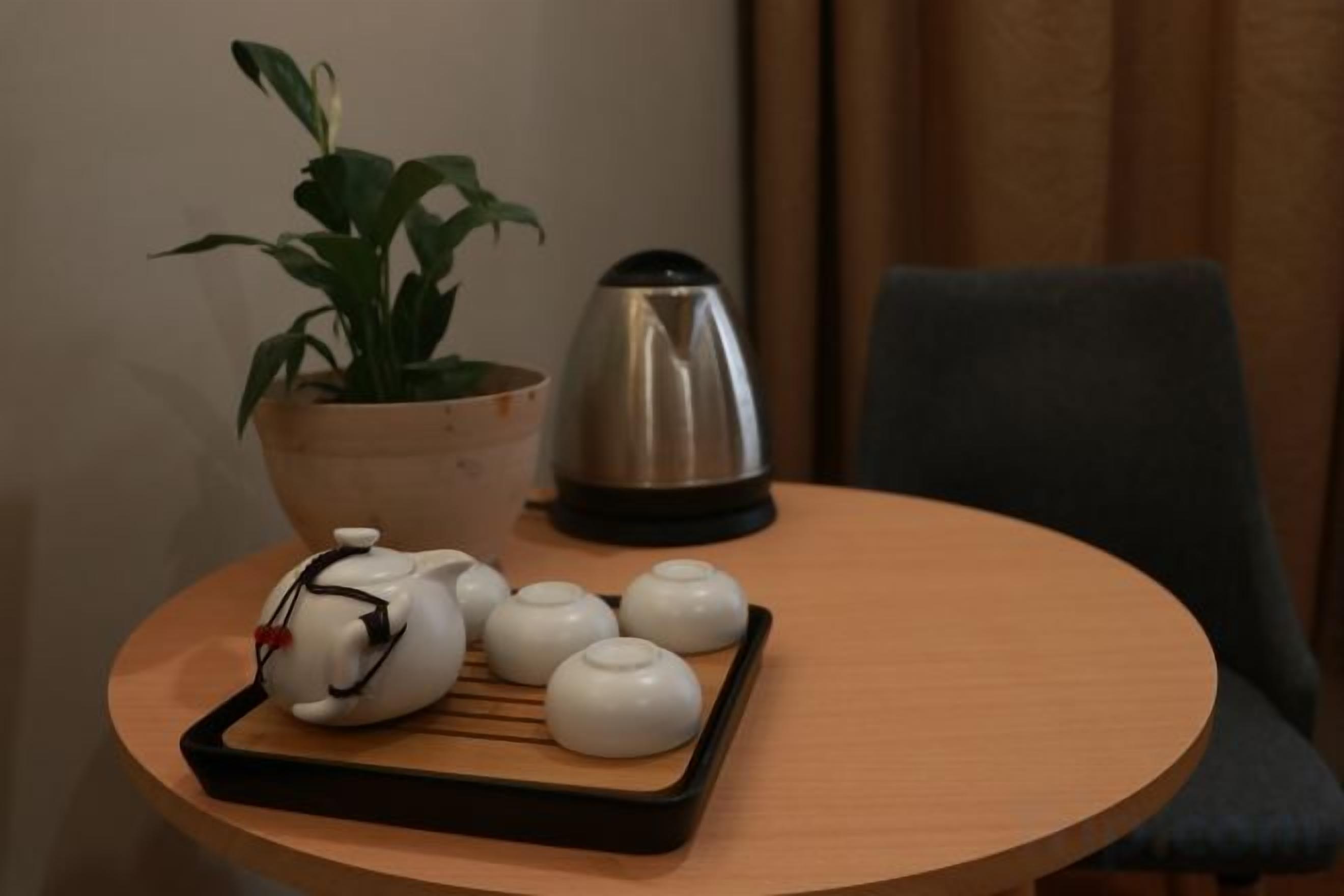 Une table ronde sur laquelle se trouvent un plateau avec des théières blanches et une théière, une plante en pot et une machine à café.