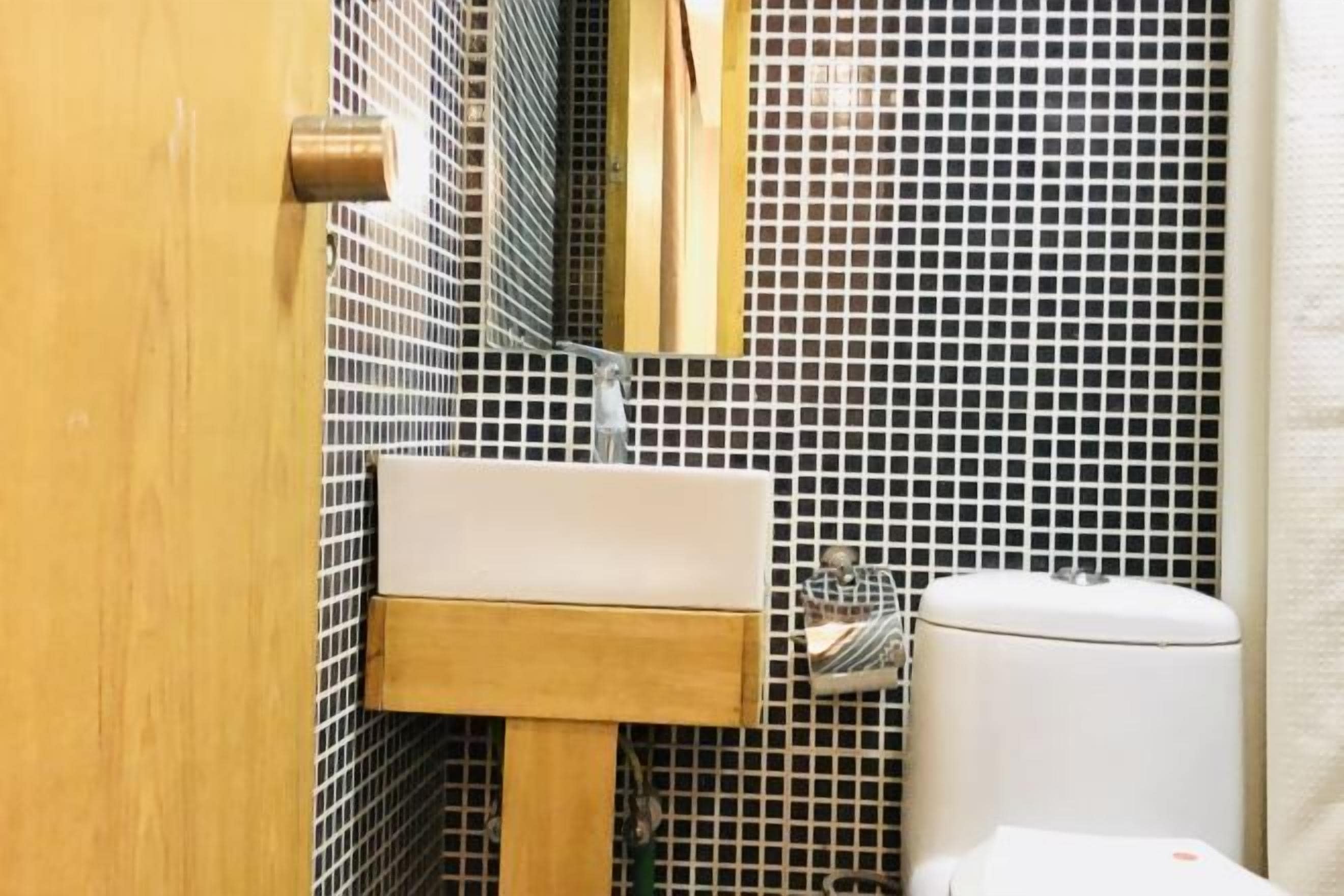 Ein Badezimmer mit Holztür, Waschbecken in Weiß, Spiegel und Toilette an einer gefliesten Wand.