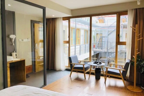 A hotel room with a bed, a small table with chairs, a window with a view of a building, and a coat rack. - Fengma Feiyang Hostel (Lhasa)