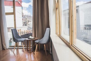 Una habitación con dos sillas, una mesita y un ventanal grande con cortinas.
