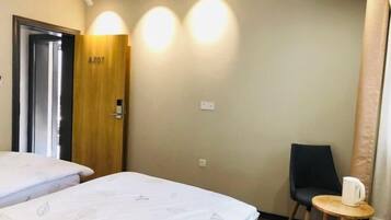 A hotel room with two beds, a wooden door labeled A207, a small table with a white mug, and a black chair.