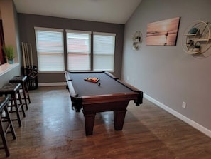 A pool table in a room with wooden flooring, two windows with blinds, and a wall-mounted shelf with decorative items. - Golfer's Dream: Pool, Spa & Patio on 18-Hole Course, one level, Luxury, comfort (Humble)