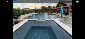 Ein Schwimmbecken mit Whirlpool, umgeben von einer Terrasse mit Liegestühlen und Sonnenschirmen.
