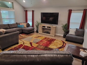 Una sala de estar con un sofá seccional, una chimenea, un televisor de pantalla plana y una alfombra estampada.