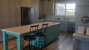 A kitchen with a central island, two bar stools, a refrigerator, and a window providing natural light. - North Shore Oasis - 5 minutes from the lake! (St. Charles)