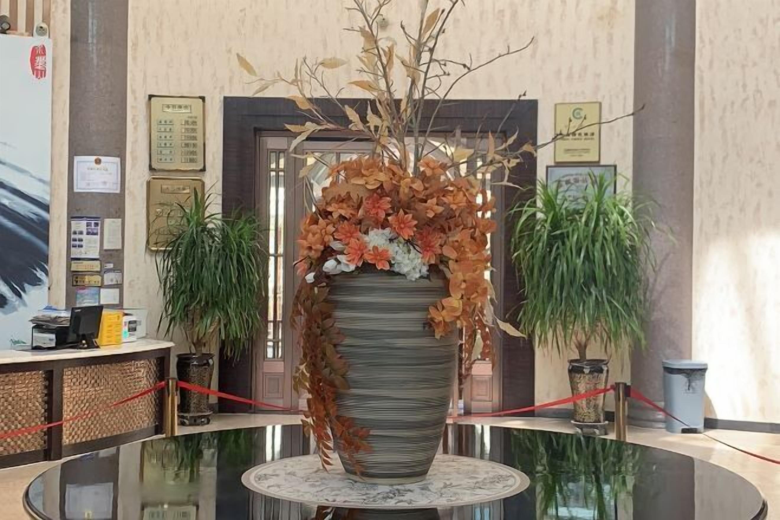 Ein Empfangsbereich mit einer großen Blumenvase, einem Empfangstresen und zwei Blumentöpfen.