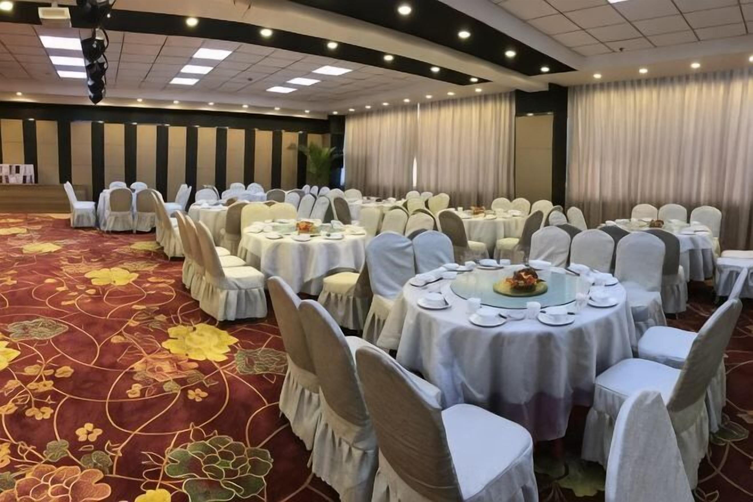 Un salón de banquetes con mesas redondas, sillas y una alfombra roja.