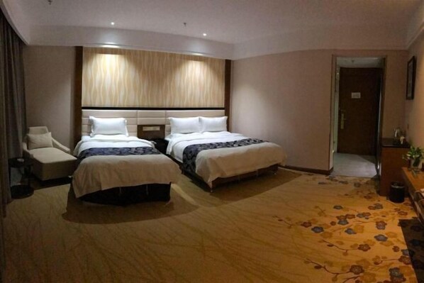 A hotel room with two beds, a sofa, a desk, and a patterned carpet.