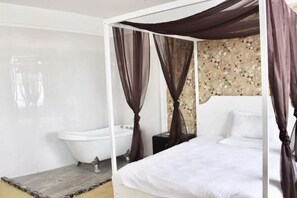 Un dormitorio con cama de dosel, una bañera blanca y suelo de madera.