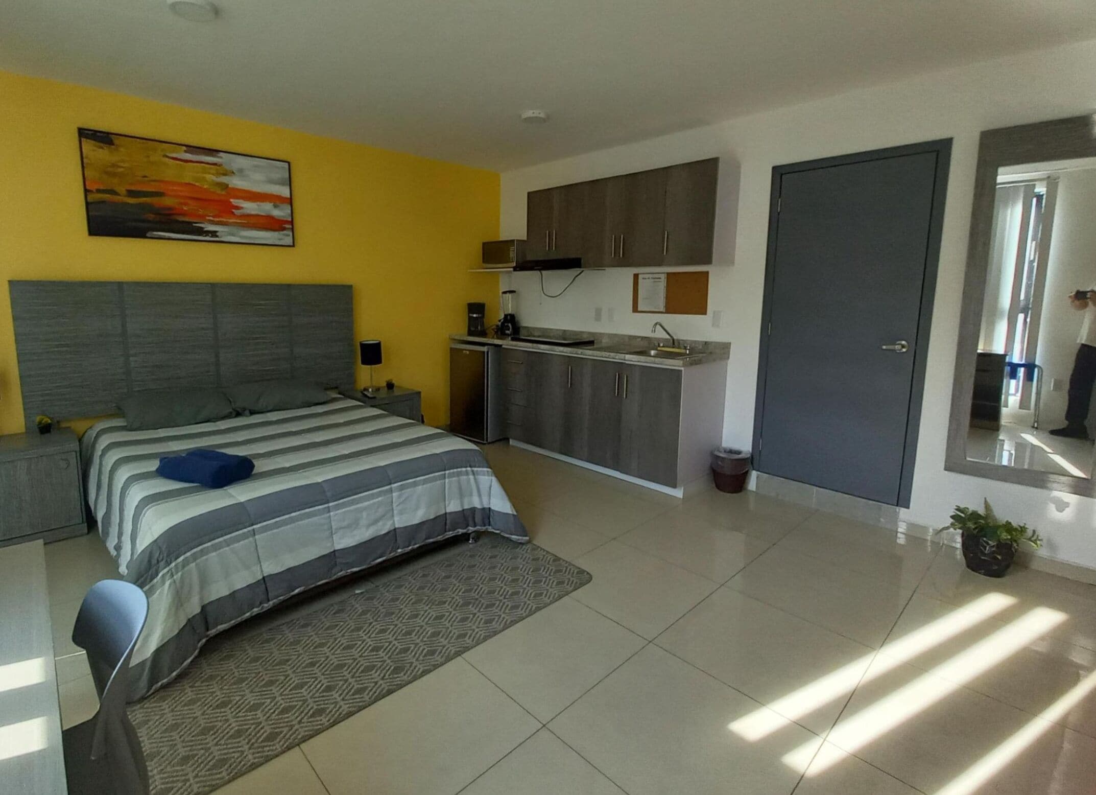 A modern bedroom with a bed, bedside tables, a small kitchenette, and a bathroom.