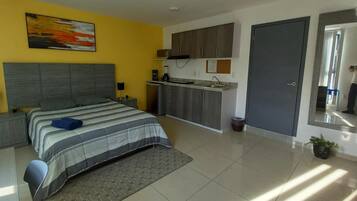 A modern bedroom with a bed, bedside tables, a small kitchenette, and a bathroom.