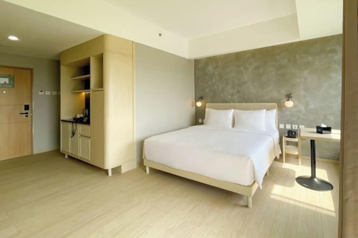 A modern hotel room with a large bed, a desk, and a wardrobe.