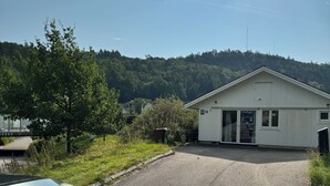 En bygning med skråt tag, en belagt indkørsel og en græsplæne med træer.