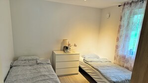Et soveværelse med to senge, et natbord med lampe, og et vindue med blomstrede gardiner.