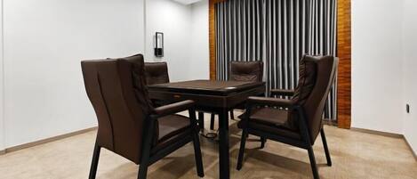 A conference room with a rectangular table and four chairs, a wall-mounted light, and a vertical curtain.