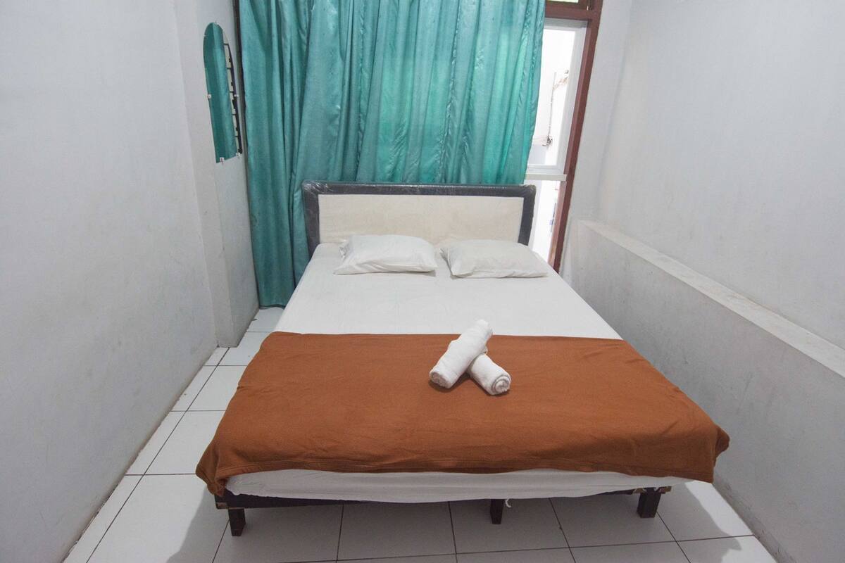 Quarto pequeno com uma cama, cortinas verde-água e cabeceira branca.