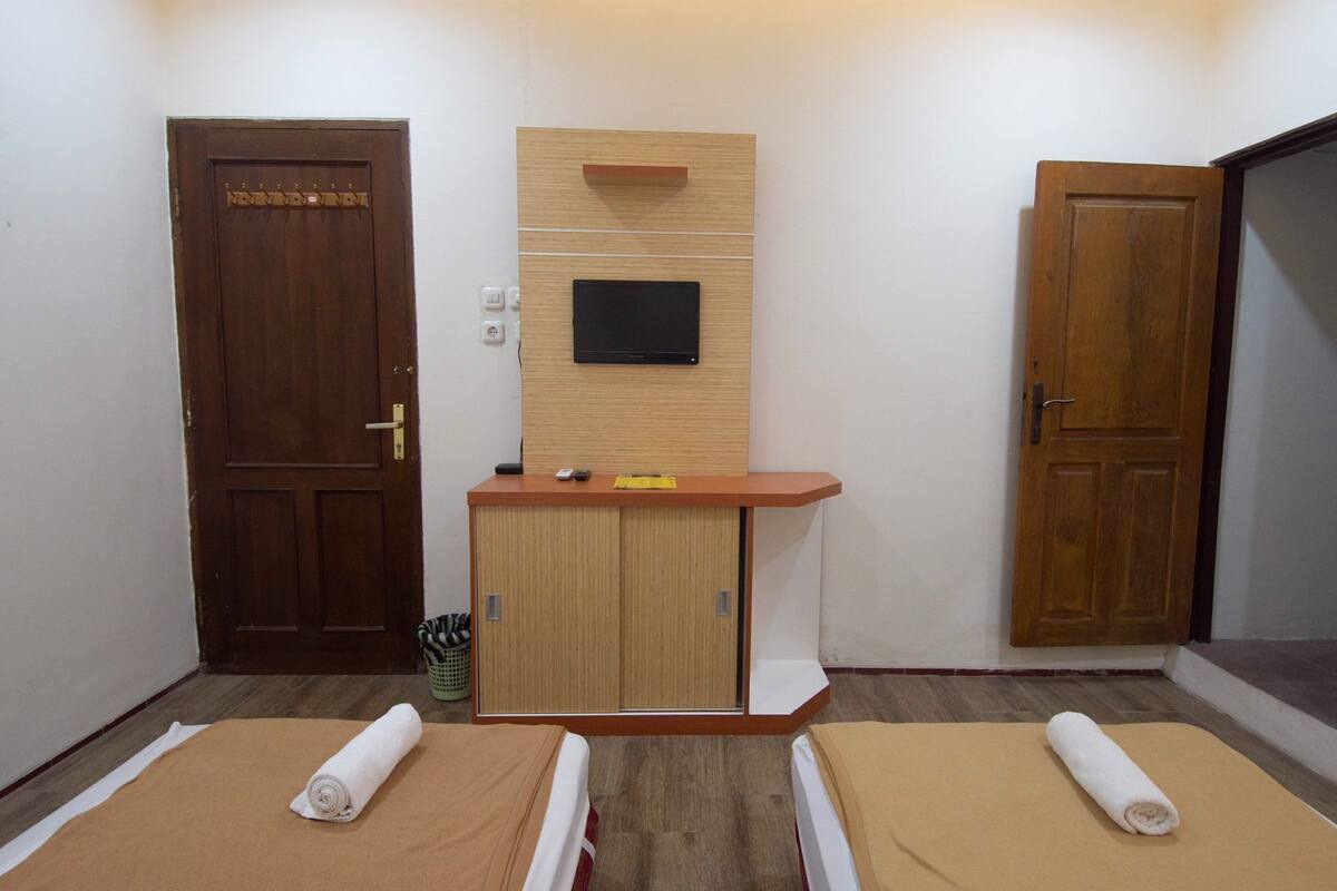 Um quarto com duas portas de madeira, um pequeno armário de madeira com uma TV de tela plana e duas mesas de massagem com toalhas.