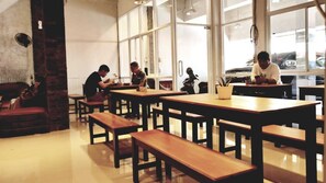 A cafe with wooden tables and benches, large windows, and a brick wall. - Simpang 7 Residence (Kudus)
