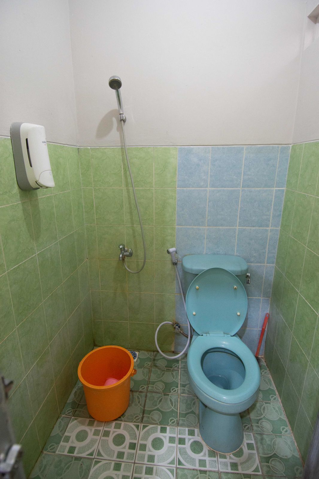 Un baño pequeño con inodoro, ducha y dispensador de jabón.