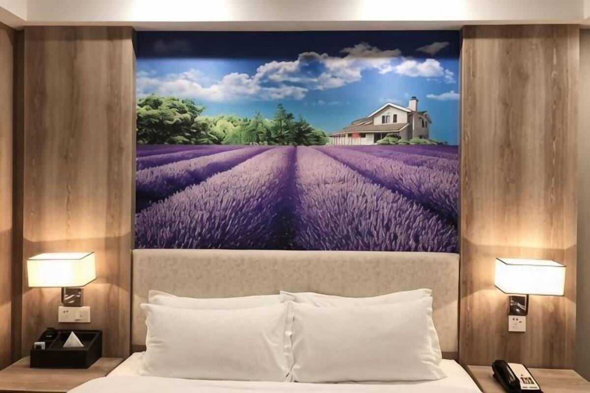 A hotel room with a bed, two bedside lamps, a nightstand, and a large wall mural of a lavender field.