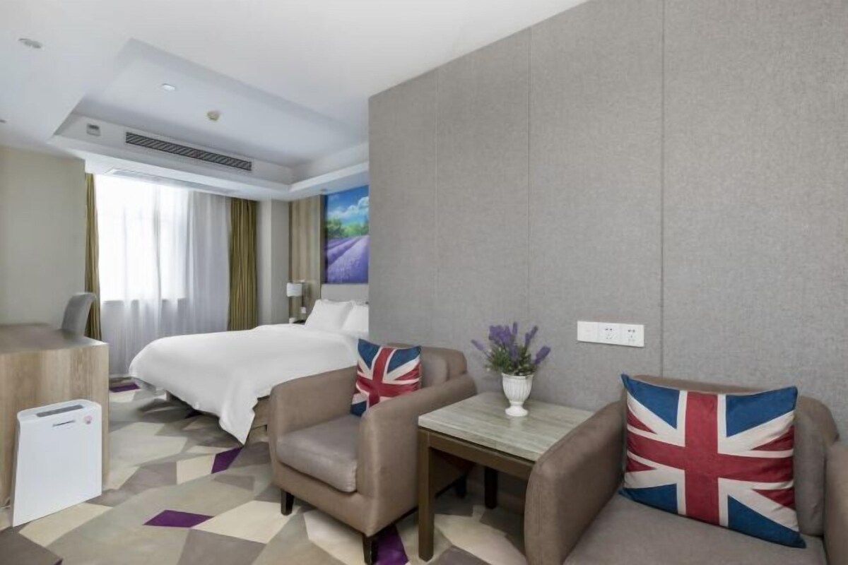 A hotel room with a bed, a desk, a chair, a small table, and a decorative pillow with a flag design.