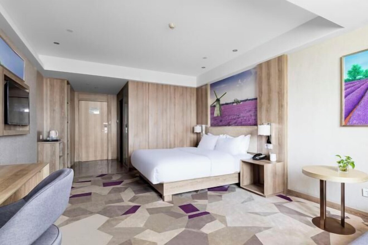 A modern hotel room with a bed, bedside table, lamp, and a painting of windmills.